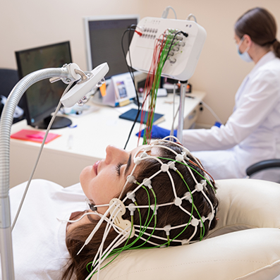 Woman with several electrodes attached to her head while a doctor looks at a computer in the background